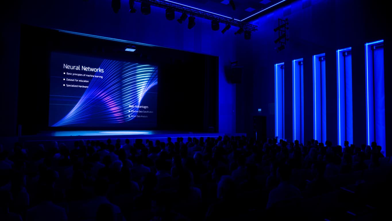 Conference audience facing a brightly lit keynote stage